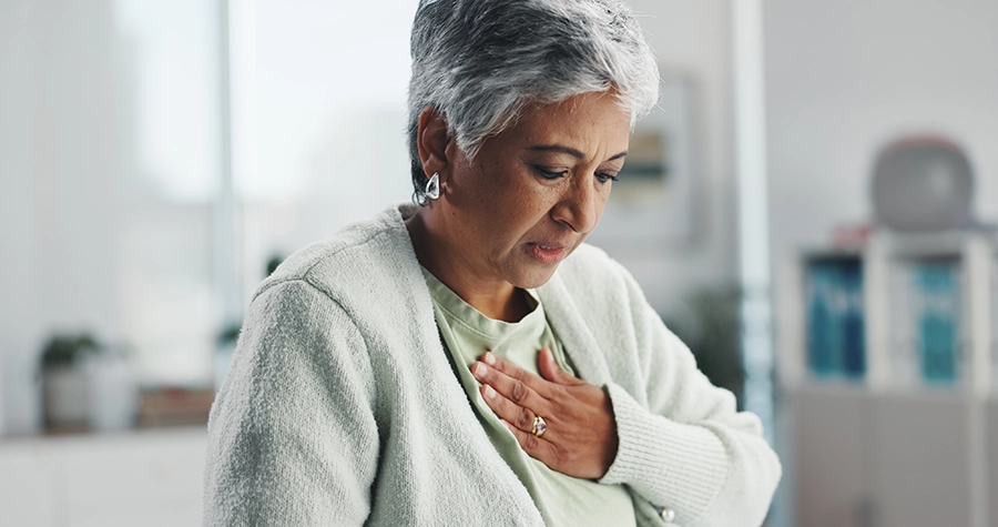 Older woman with short gray hair holds a hand to her chest and looks down, appearing to feel chest discomfort.
